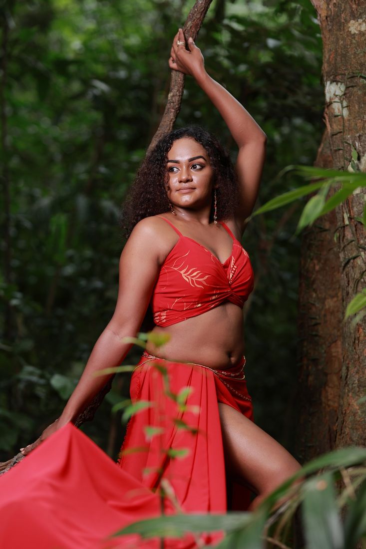 Model in red reaching up to a branch in the rainforest